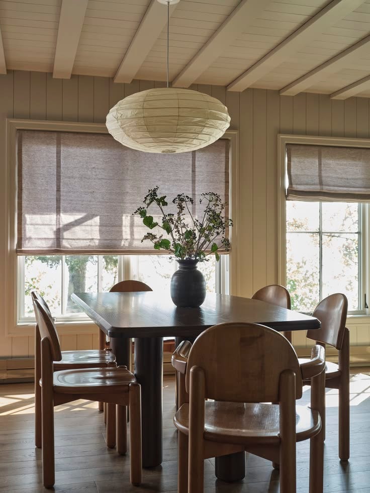 This may contain: a dining room table and chairs in front of two windows with shades on the window This may contain: a dining room table and chairs in front of two windows with shades on the window