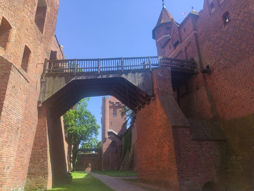 A wooden bridge joins two sections of the castle. It is viewed from below, unreachable from here and at about the level of the 3rd storey.