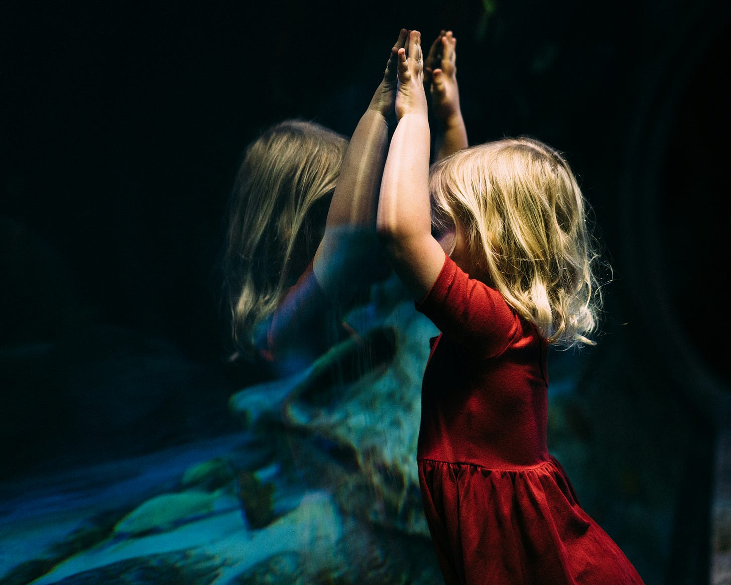 Young girl leaning against a fish tank with her hands raised over her head