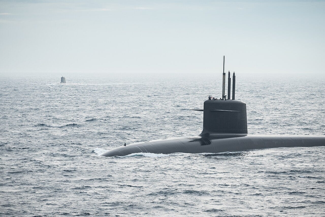 A dark French ballistic missile submarine running on the surface in grey Atlantic water, its sail and masts raised, with a second submarine sail visible in the distance. A dark French ballistic missile submarine running on the surface in grey Atlantic water, its sail and masts raised, with a second submarine sail visible in the distance.