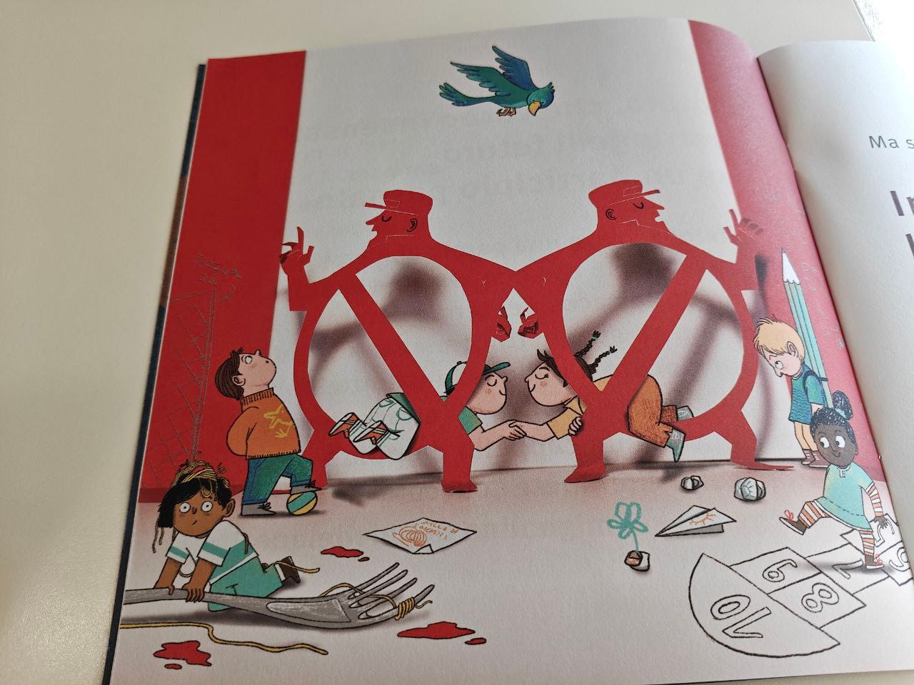 Illustrazione a pagina intera da un libro, con una complessa scena composta da figure e bambini. Due grandi figure rosse, ritagliate in silhouette e somiglianti a due vigili o militari stilizzati che si tengono per mano, formano la forma di una 'V' centrale capovolta. Diversi bambini, disegnati con tratti morbidi e colori terrosi, interagiscono con questi ritagli. Un bambino è appeso al ritaglio rosso, mentre altri due si chinano in mezzo. Una bambina è seduta in primo piano, affiancata da una grande forchetta da tavola e da alcune macchie rosse che sembrano sangue o vernice. Altri bambini sono in piedi o in ginocchio, uno dei quali tiene una grande matita. Il pavimento è cosparso di piccoli oggetti, tra cui pezzi di carta, sassi e una pista per la campana. In alto, un uccello verde con dettagli blu vola sopra le figure rosse. Lo sfondo della pagina sinistra è rosso brillante.