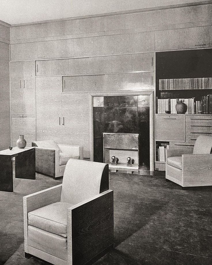 This may contain: a black and white photo of a living room with chairs, bookshelves and cabinets
