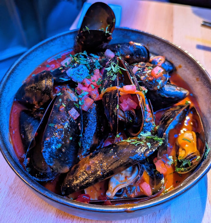 Left to right: Gambas al Ajillo (shrimps in red sauce with bread on the side); 'Nduja mussels (black mussel shells in red broth, topped with pickled red onions and herbs)