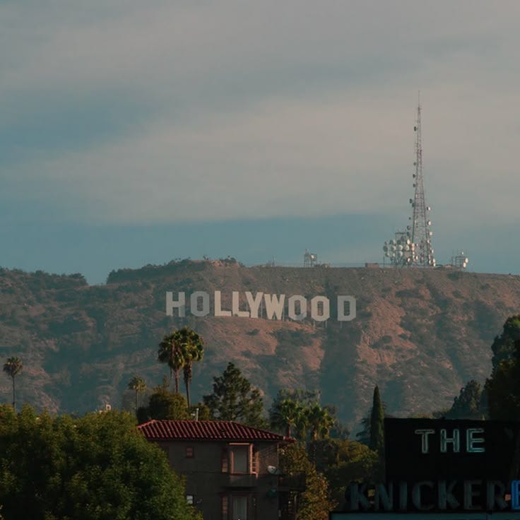 This may contain: the hollywood sign is on top of a hill in front of palm trees and mountains