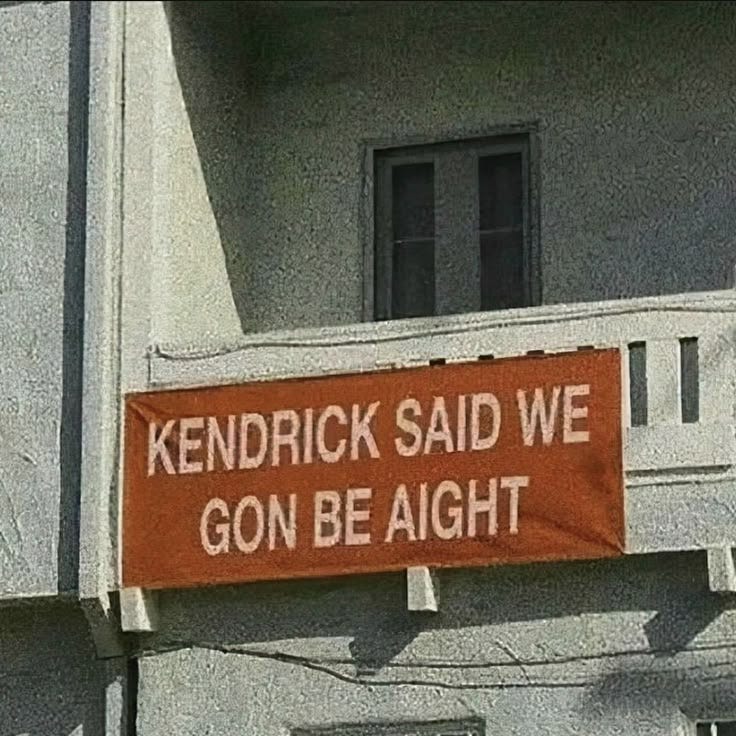 This may contain: an orange sign hanging from the side of a building that says, kendrick said we go be alright