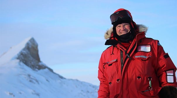 Man wearing red parka and snow gear smiling at camera from sunny Arctic landscape Man wearing red parka and snow gear smiling at camera from sunny Arctic landscape