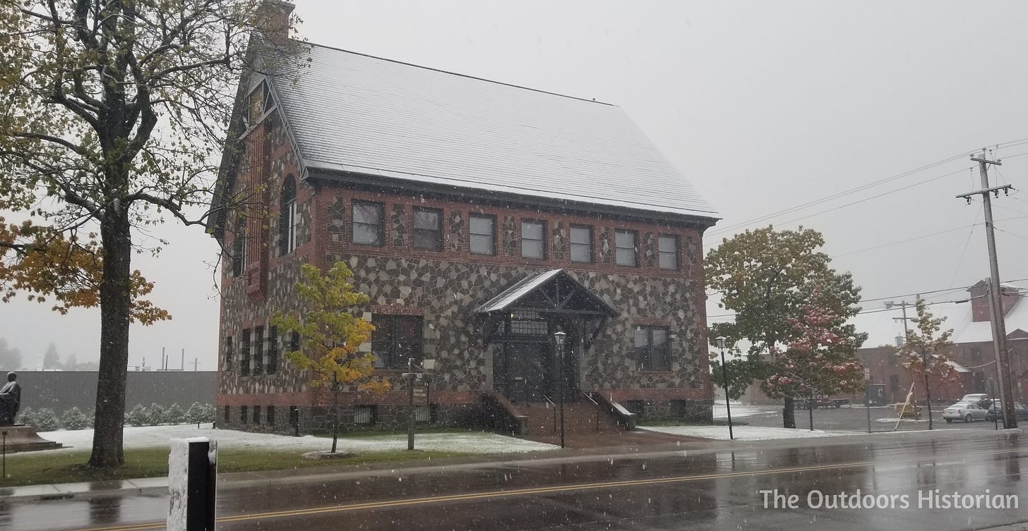 The historic Calumet and Hecla Public Library building, constructed of dark stone and brick, during a day where autumn leaves meet early lake effect snow.