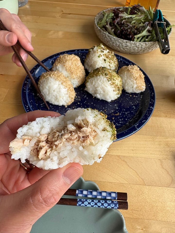 A plate of onigiri on a blue and white speckled serving plate, held up, with a dining table and fireplace in the background. A close up of an onigiri with a bite missing, showing the tuna filling.