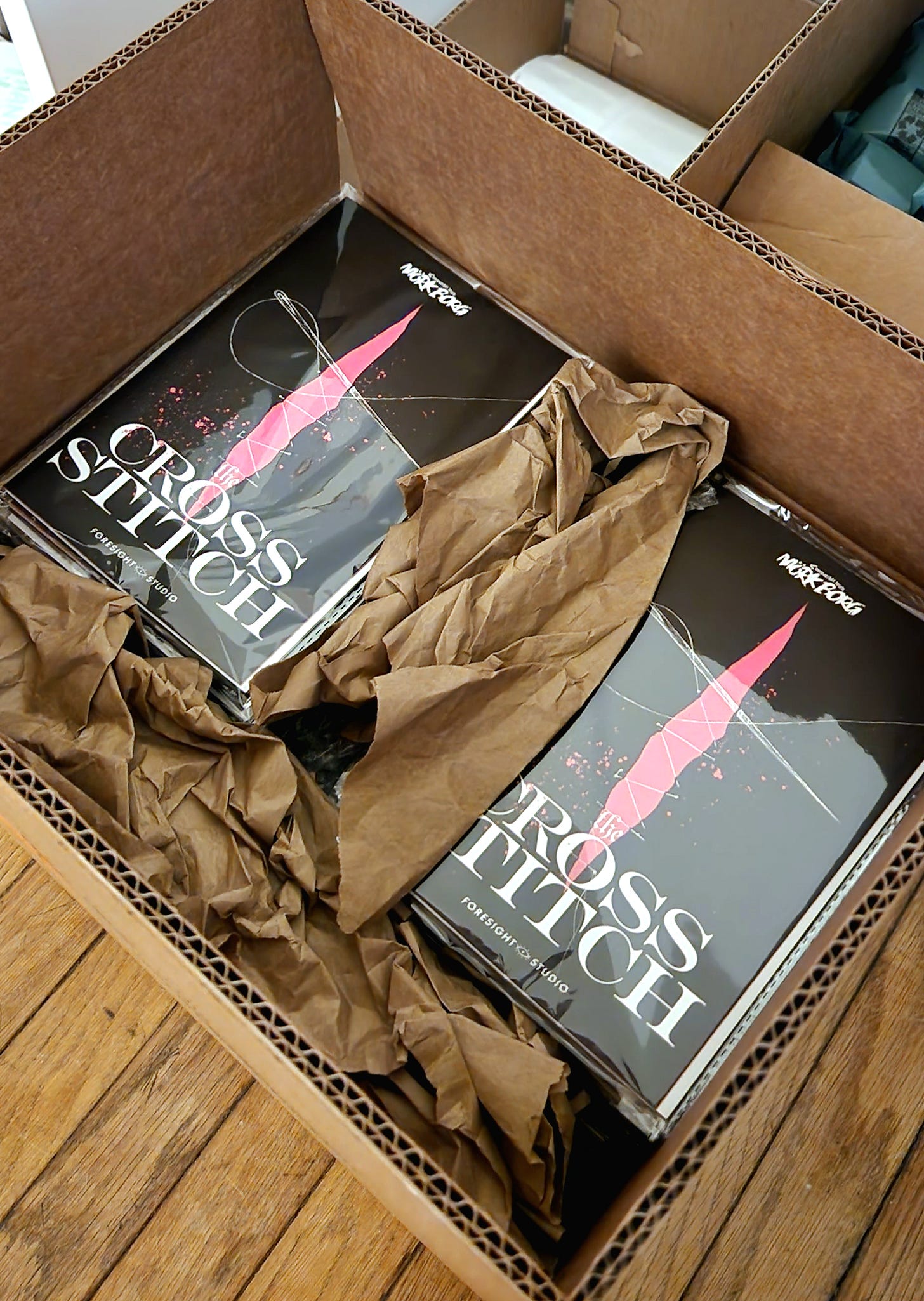 Copies of The Cross Stitch, packed and wrapped, in a large cardboard box.