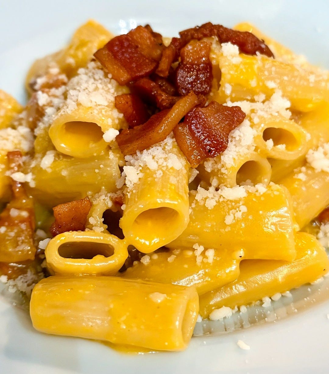 A white plate topped with pasta and bacon