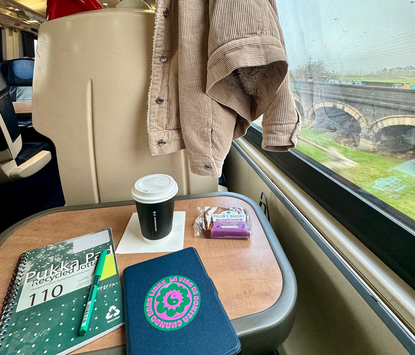 Photo of a train table with a notebook, pen, kindle and coffee cup
