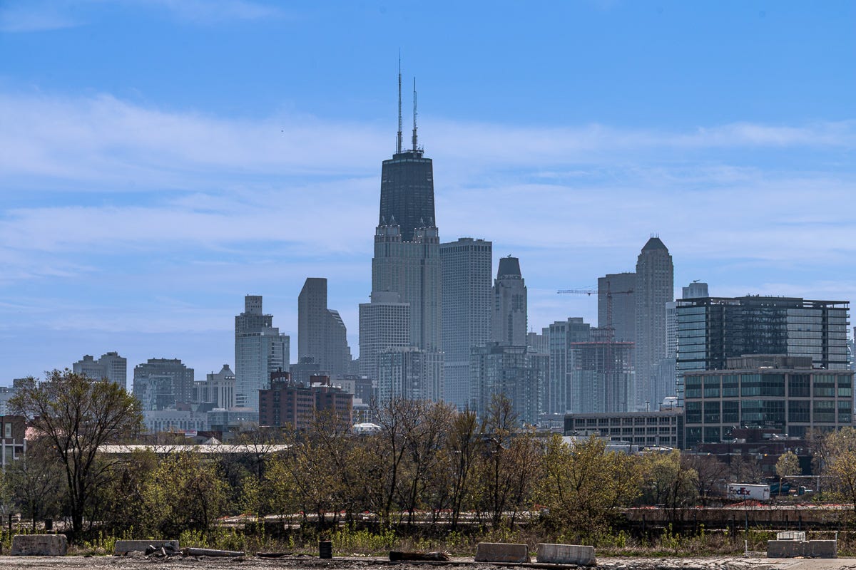 Panoramic view of the Chicago skyline including the John Hancock Center, with a foreground of trees, fences, and industrial debris. Panoramic view of the Chicago skyline including the John Hancock Center, with a foreground of trees, fences, and industrial debris.