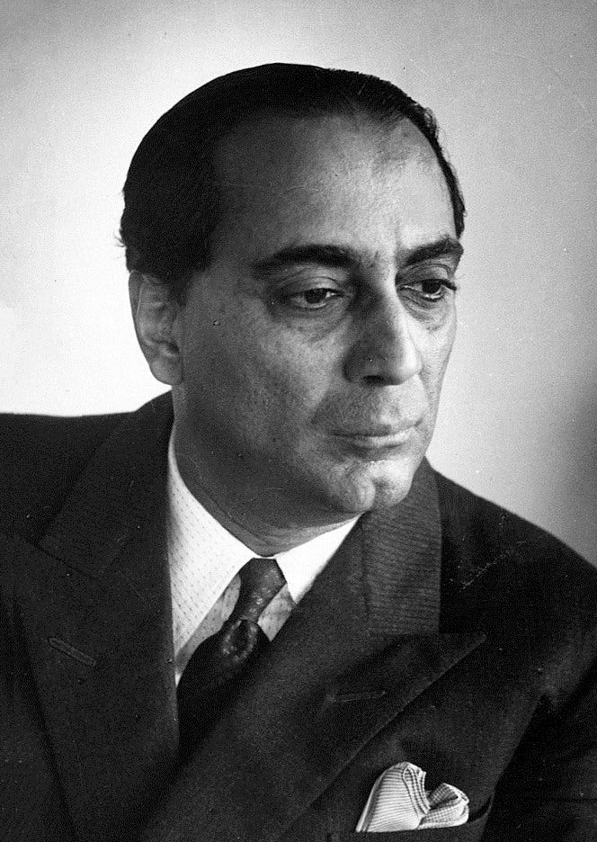 Black and white studio portrait of Homi Bhabha in a dark suit and tie, looking down and to one side