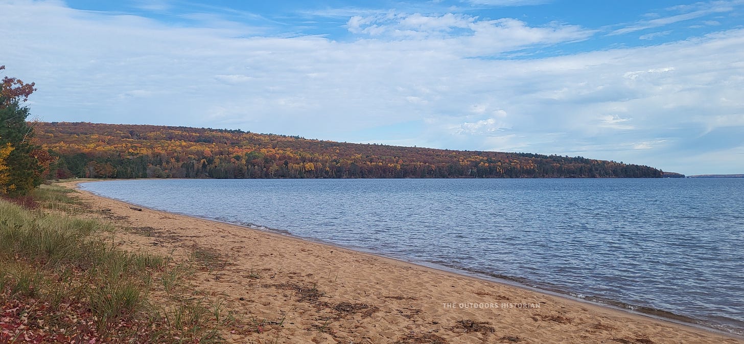 A view of the Bayfield Peninsula's fall colors from the sandy beach at Friendly Valley under a sunny sky with wispy clouds.