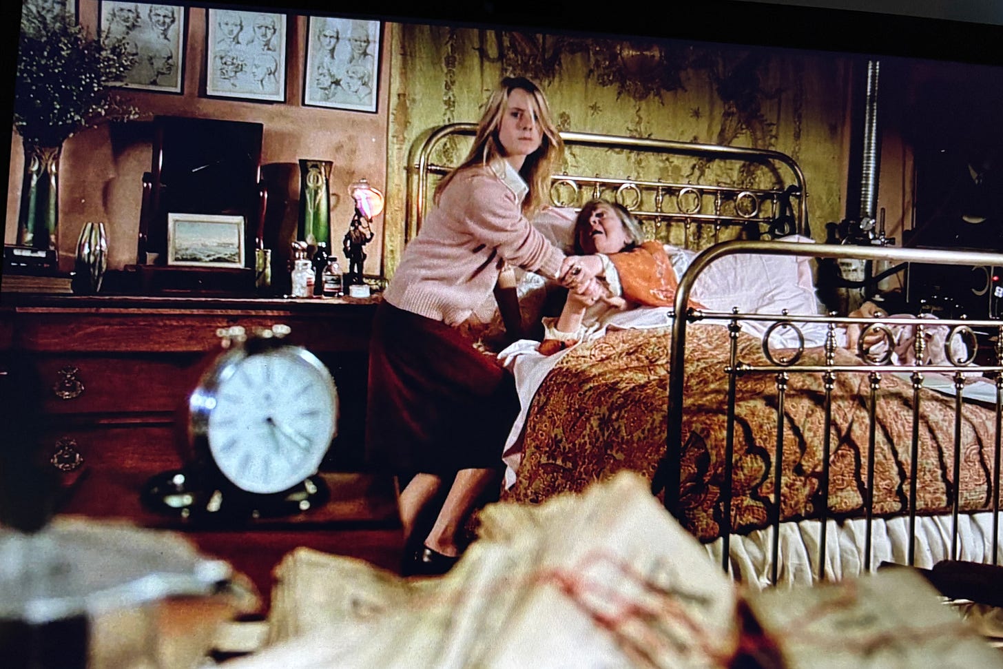 photo still from Black Moon of young woman fighting away an old woman in bed behind an alarm clock