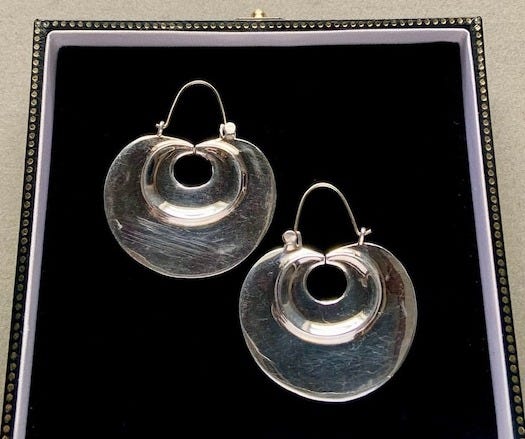 May include: A pair of silver hoop earrings with a double circle design. The earrings are displayed in a black velvet jewelry box.