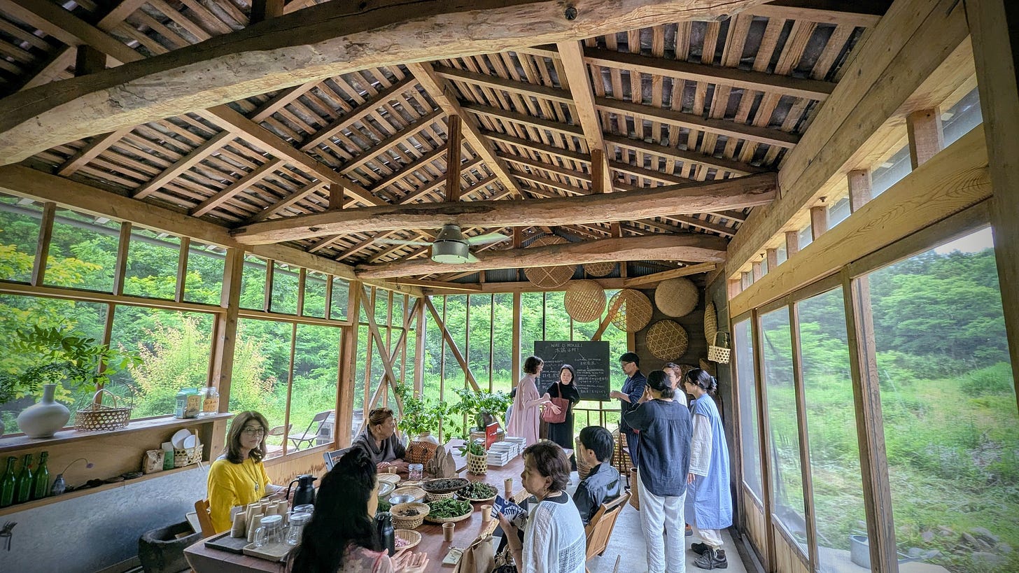 People gather around a large table inside an open-air building with thick wooden ceiling beams.