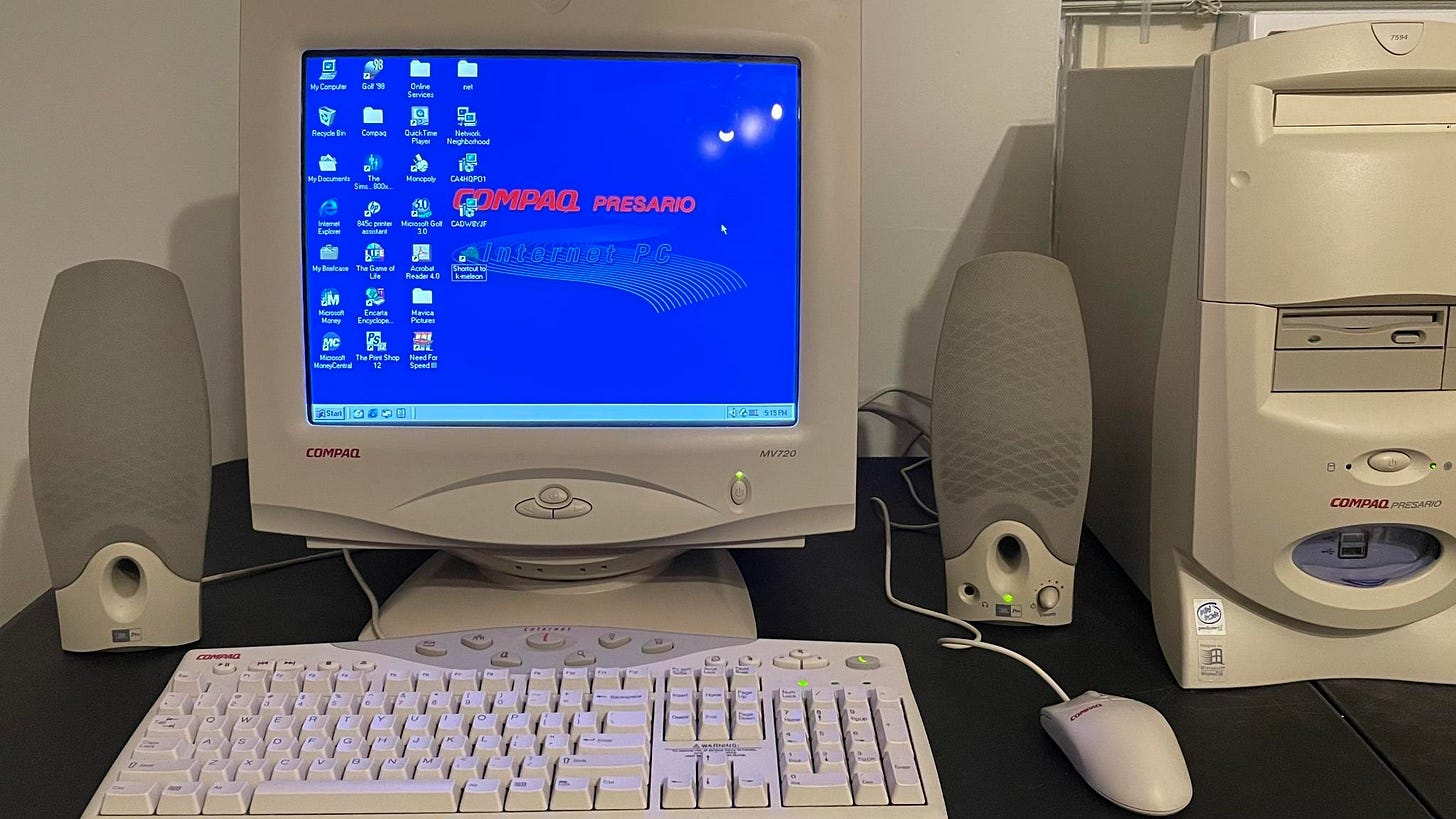 A 2000  Compaq Presario desktop computer sits on top of a desk. A keyboard sits in front of a monitor with speakers on either side. To the right is the computer tower,.