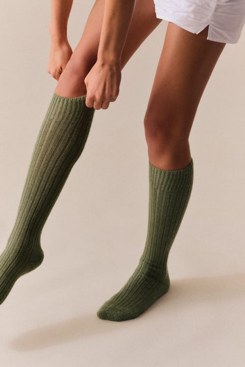 Person wearing green wool knee high socks on a plain background