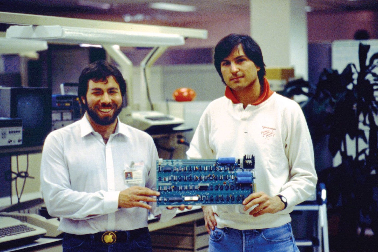 Steve Wozniak and Steve Jobs holding the Apple I circuit board in an office setting.