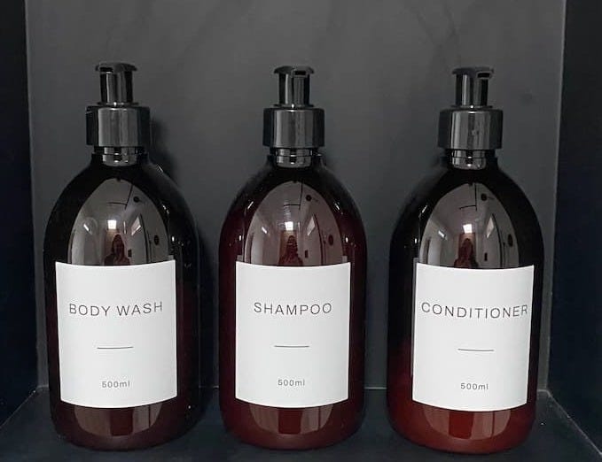 three dispenser bottles in dark amber with black tops and white labels