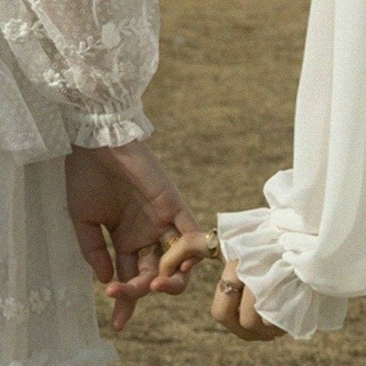 This may contain: two people are holding hands and touching each other's fingers in an open field