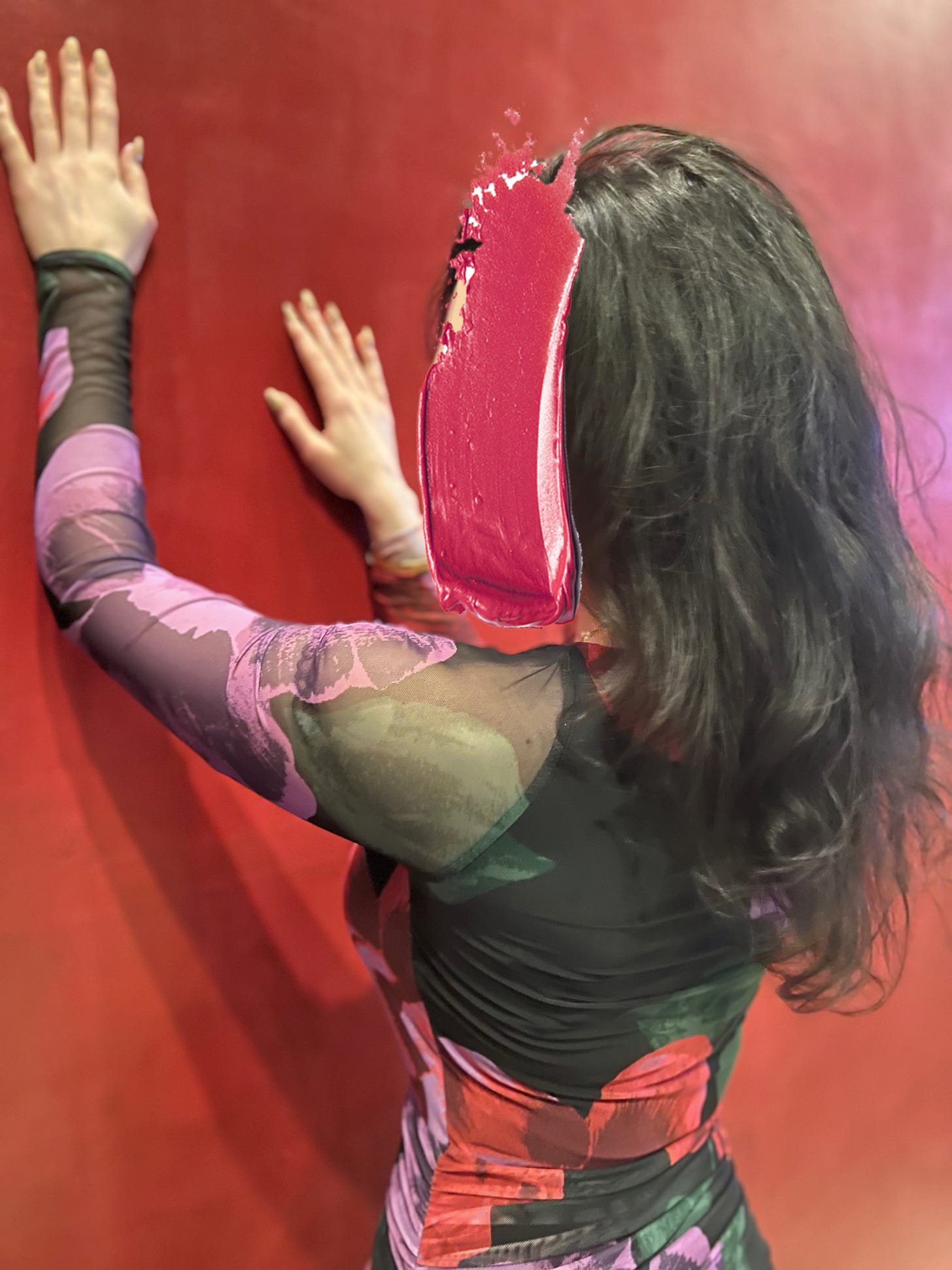 Chicago provider Elena Marchetti posing against a red wall, hands on the wall, in a form-fitting red and purple flowered dress, brunette hair flowing in soft waves