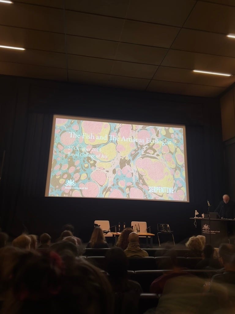 Photo taken in a dimly lit lecture theatre at the RCA with people in seats looking towards the stage for an event called āThe Fish and The Artist as Ecologist.ā Photo taken in a dimly lit lecture theatre at the RCA with people in seats looking towards the stage for an event called āThe Fish and The Artist as Ecologist.ā