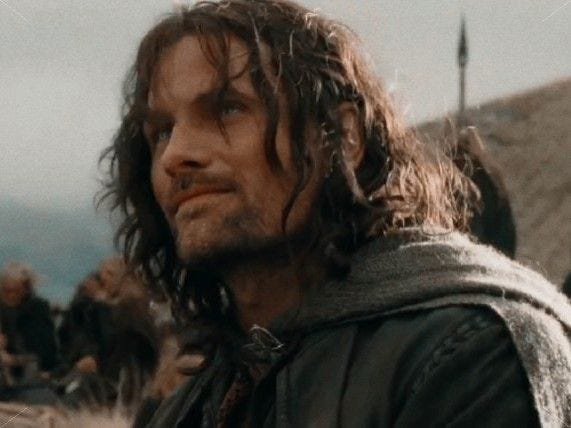 This may contain: a man with long hair standing in front of other men and looking off into the distance