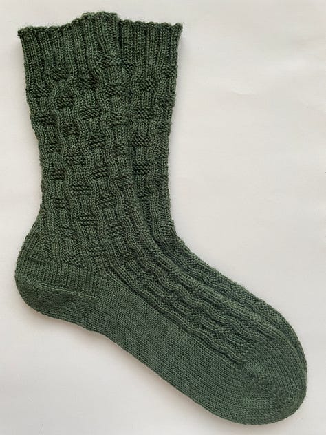 A green hand knit sock with a basket weave pattern.
