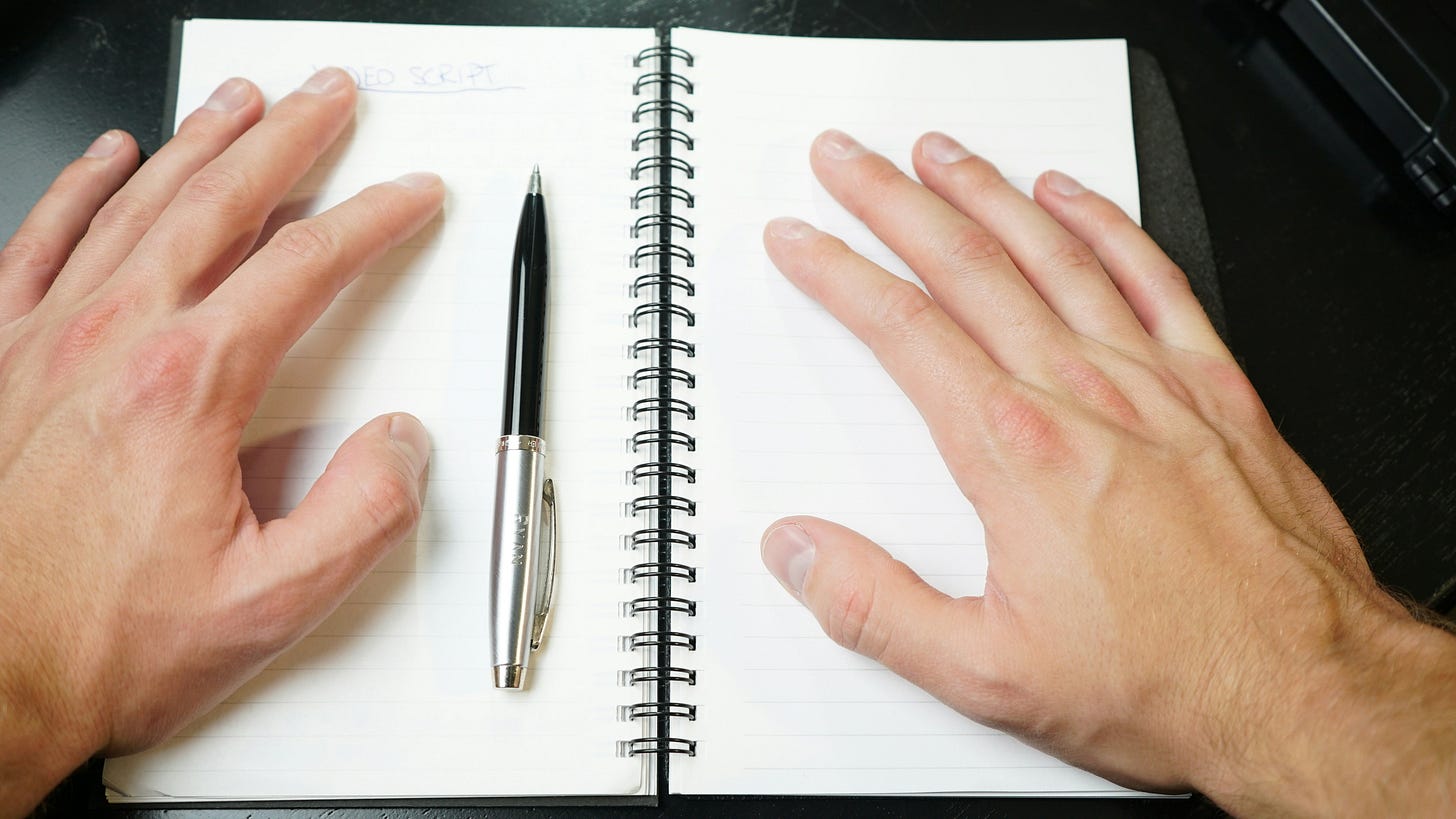 Two hands rest on either side of an open blank notebook, with a pen centered on the page. The image captures a quiet moment before writing begins. Two hands rest on either side of an open blank notebook, with a pen centered on the page. The image captures a quiet moment before writing begins.