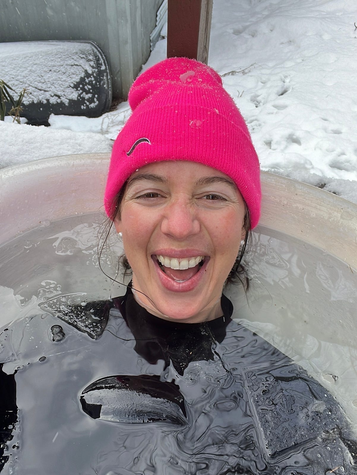 Kate smiles in a cold plunge tub in winter, wearing a wetsuit and a hot pink beanie hat. Kate smiles in a cold plunge tub in winter, wearing a wetsuit and a hot pink beanie hat.