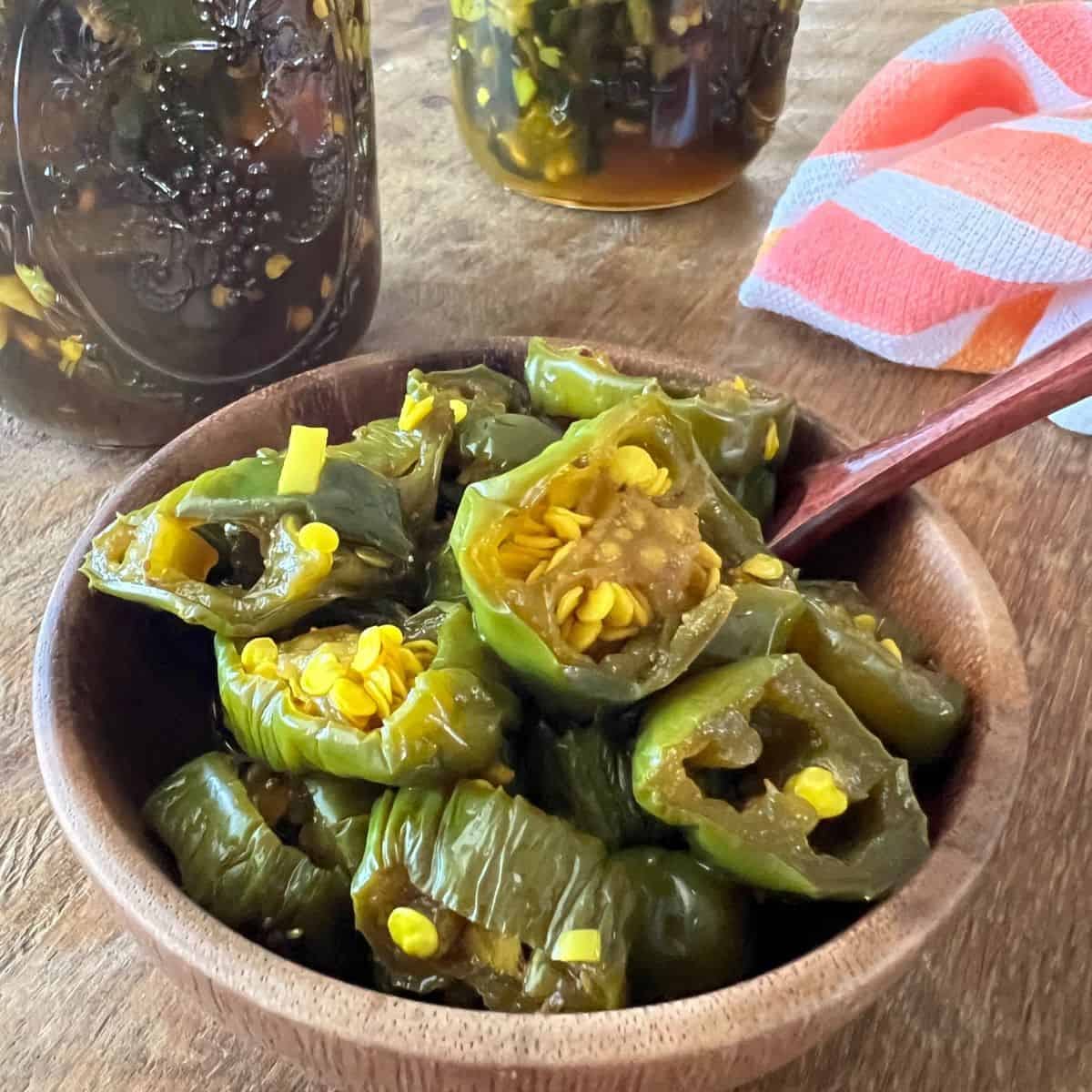 Wooden bowl full of candied jalapenos with acnned jars of cowboy candy in the background