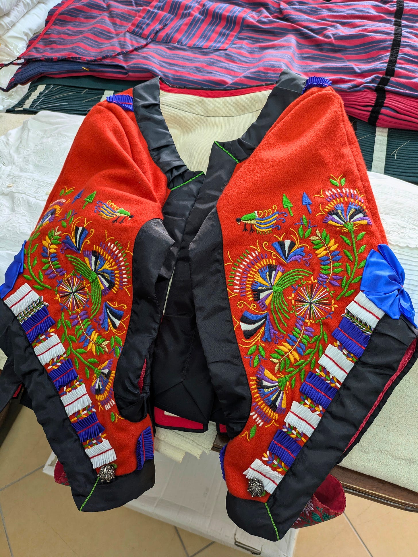 Brightly colored traditional garment featuring floral embroidery, geometric patterns, and decorative ribbons, laid out on a table.