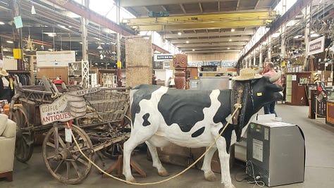 Pictures of random furniture, trunks, statues, lamps, stained glass windows, and a cart and fake cow from a warehouse that sells repurposed, salvaged items.