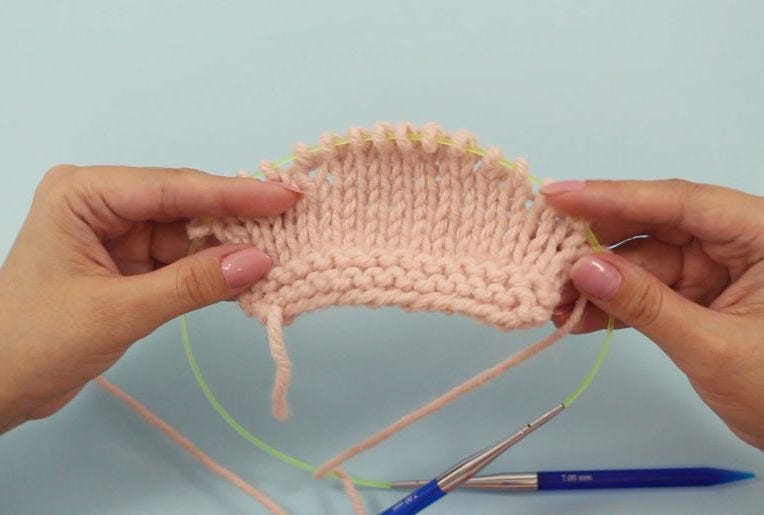 hands holding a pink knitting swatch with short rows