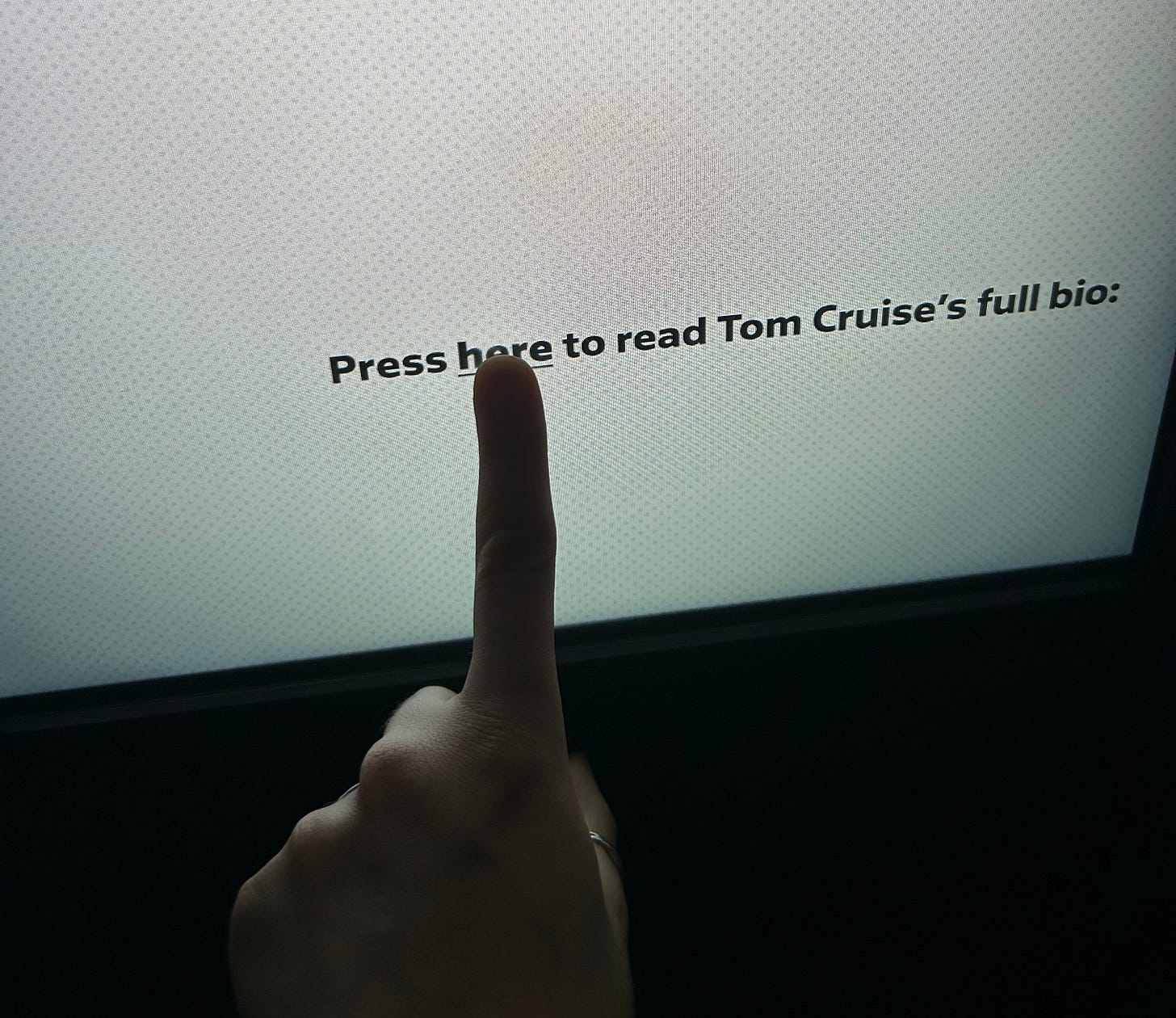 a finger pressing a button on a white screen with text that reads 'press here for Tom Cruise's full bio'