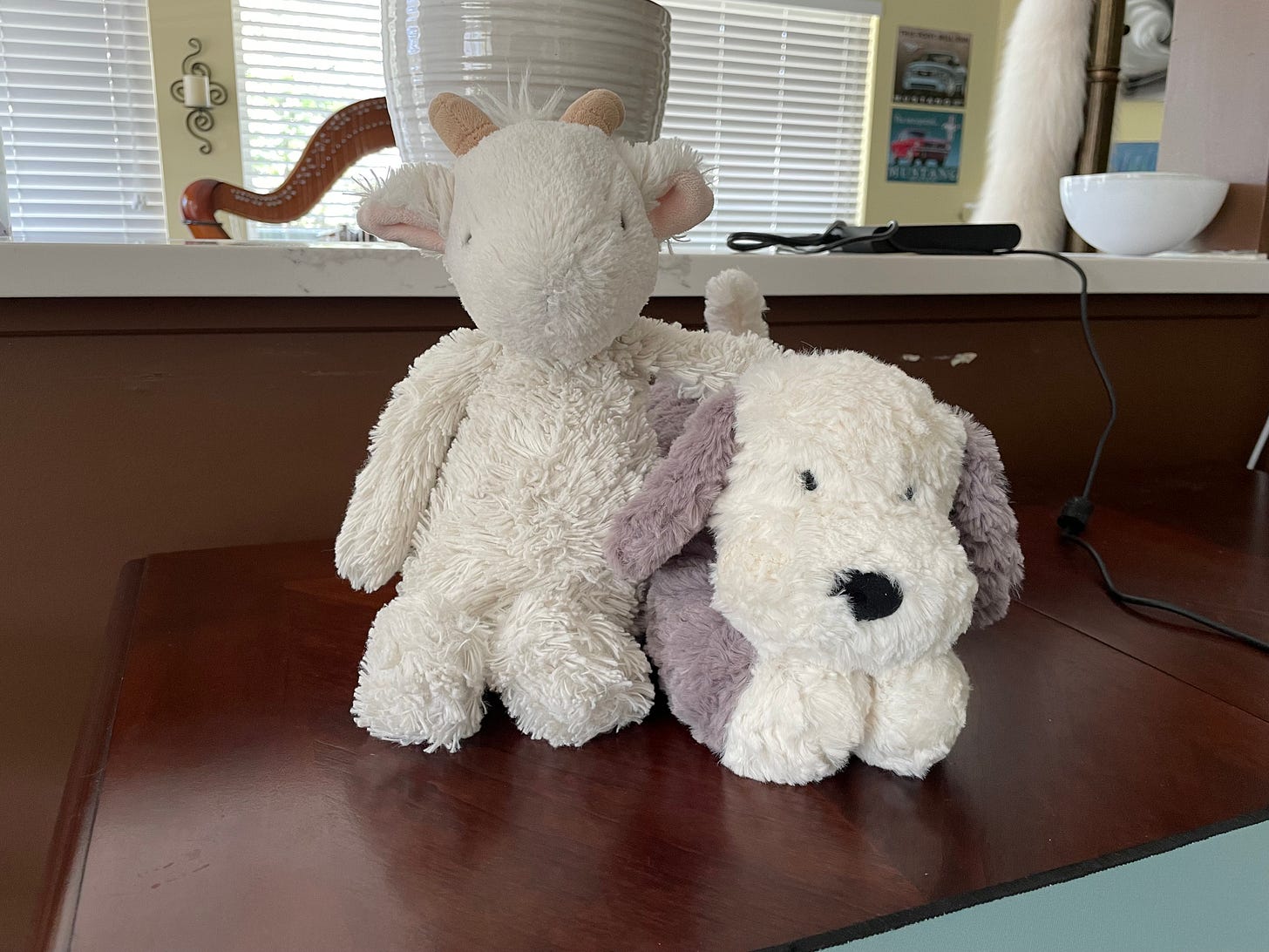 A stuffed white goat and a stuffed grey and white puppy sit on a wood table
