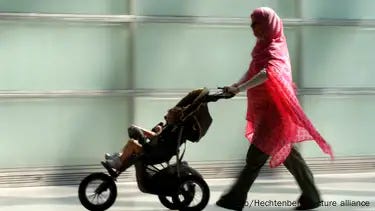 A woman wearing a red headscarf is seen pushing a pram with a small child in Berlin A woman wearing a red headscarf is seen pushing a pram with a small child in Berlin
