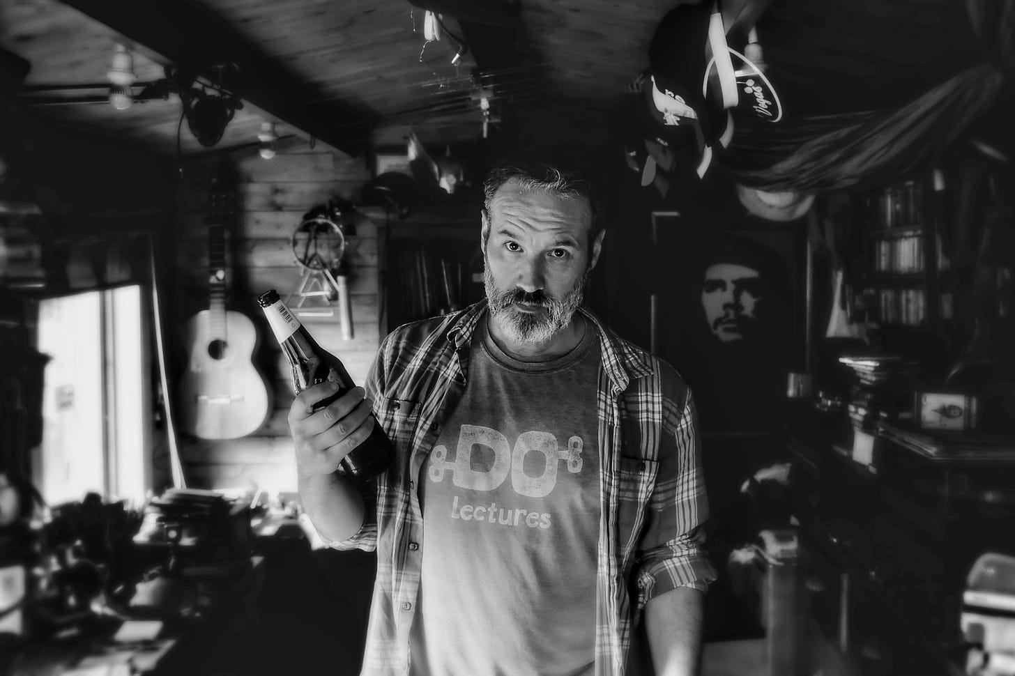 A photo of me looking semi seriously into the camera which is hanging off a rubber sucker on my shed window. In my hand, I have a beer I found in the fridge which was left over from a party.