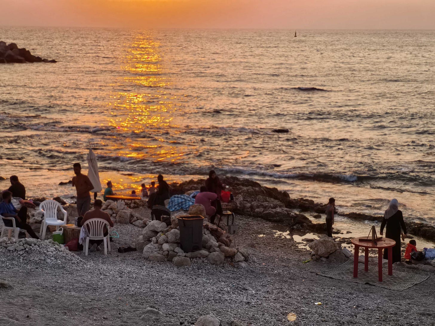 People relaxing in chairs by the ocean at sunset.