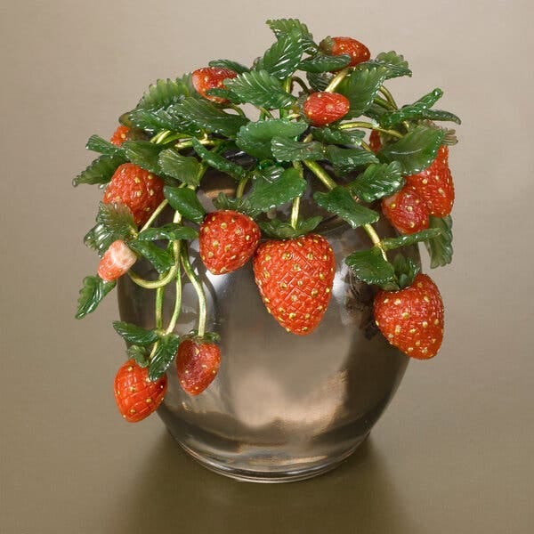 A silver-colored bowl holding what looks like a strawberry bush. The fruits are made of red coral, their leaves of green jade.