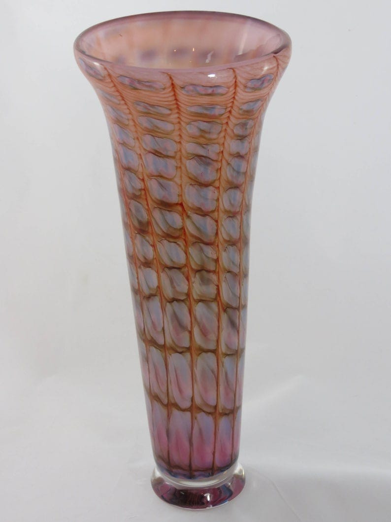 May include: A tall, clear glass vase with a pink, brown, and white swirl pattern. The vase has a wide mouth and a narrow base.