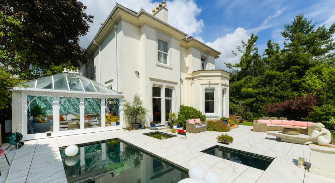 A white house with a conservatory and pool in front of it A white house with a conservatory and pool in front of it
