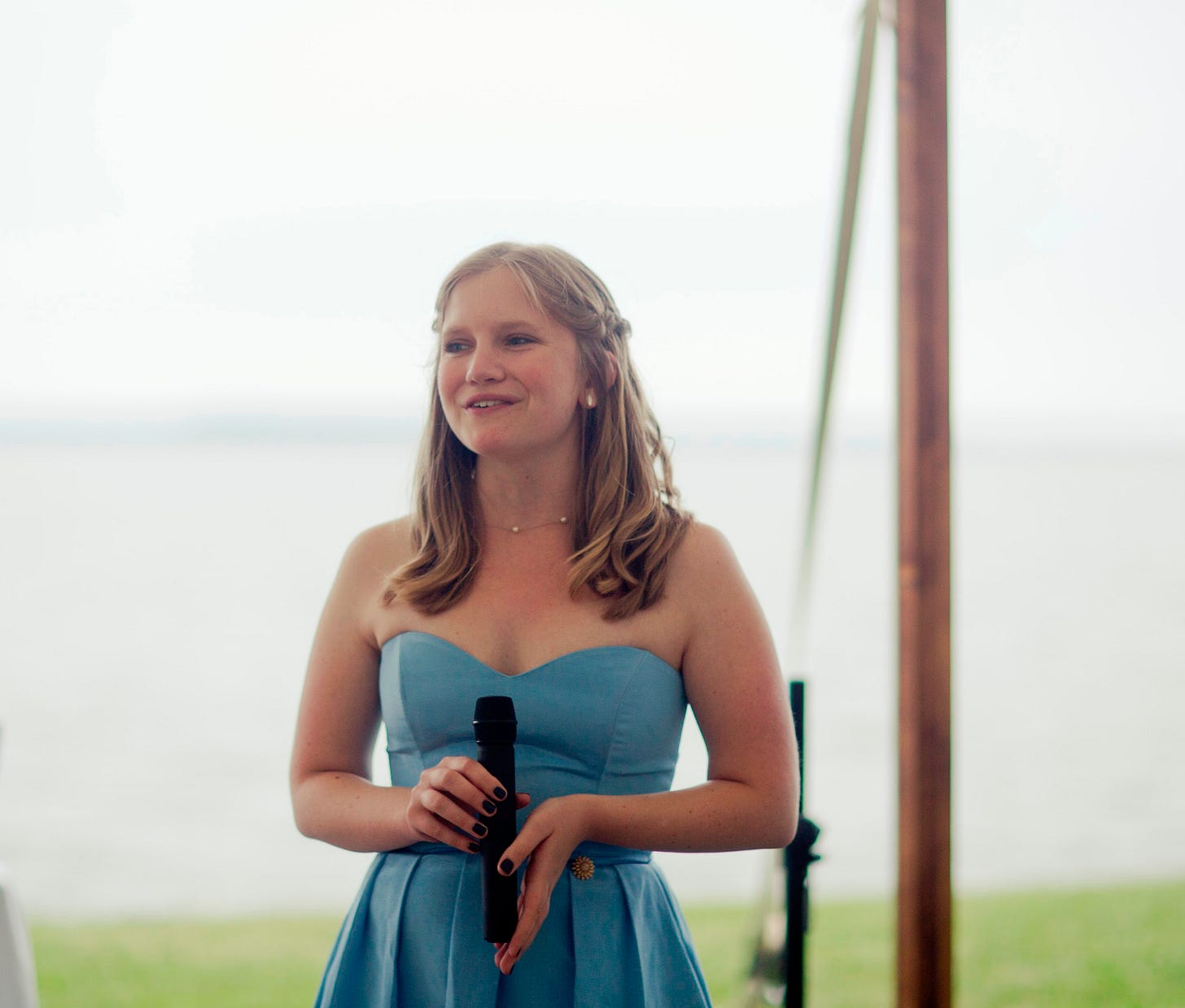 The author at 24, giving a speech at her friend's wedding in a blue dress
