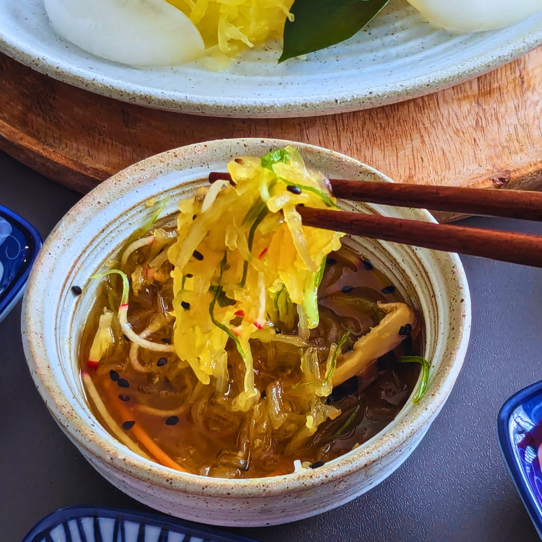 Close-up of spaghetti squash somen strands mixed with tsuyu and colorful toppings, lifted by chopsticks over a dipping bowl.