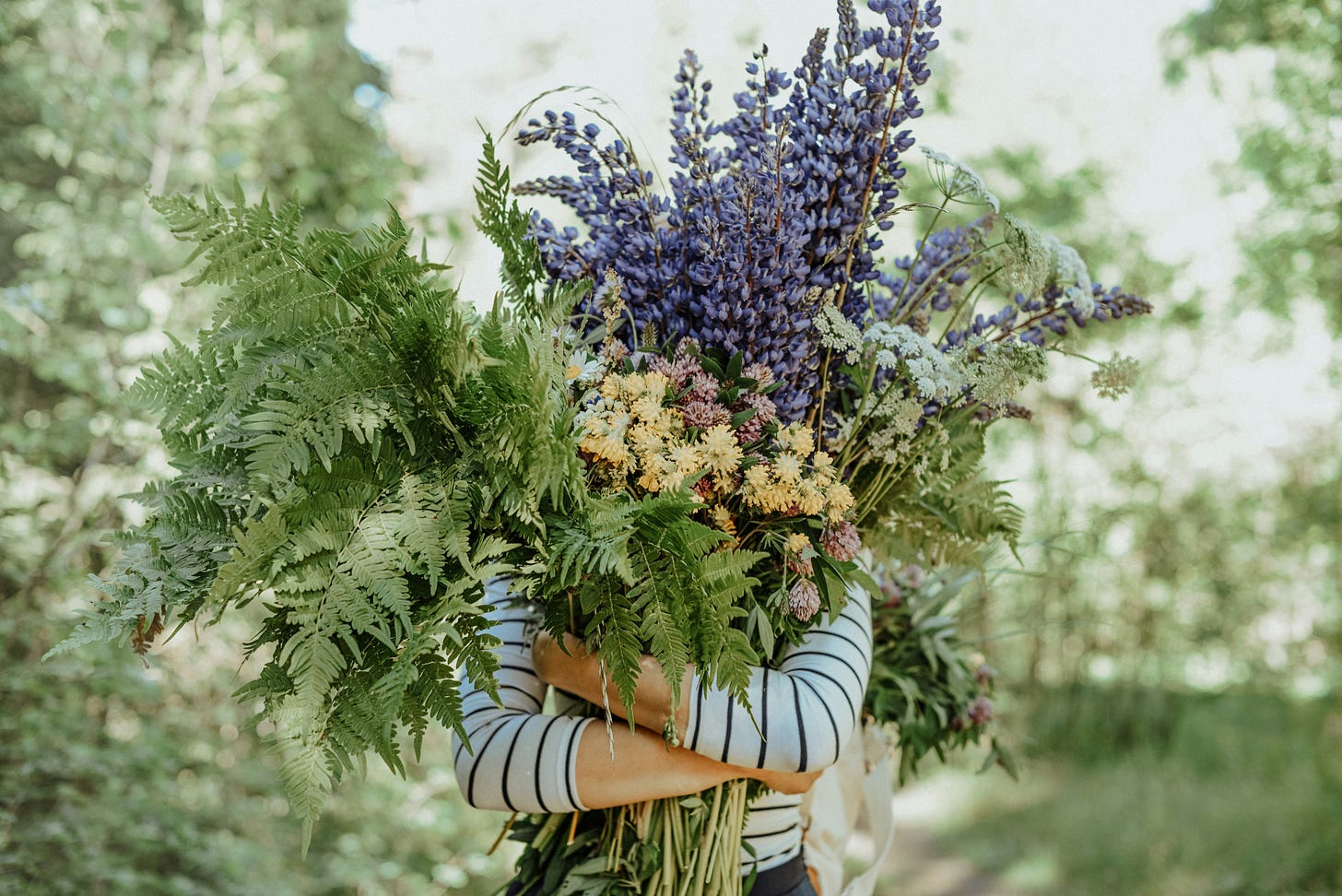 photo of person holding large bunch of flowers and ferns that cover their face, green in backgroud