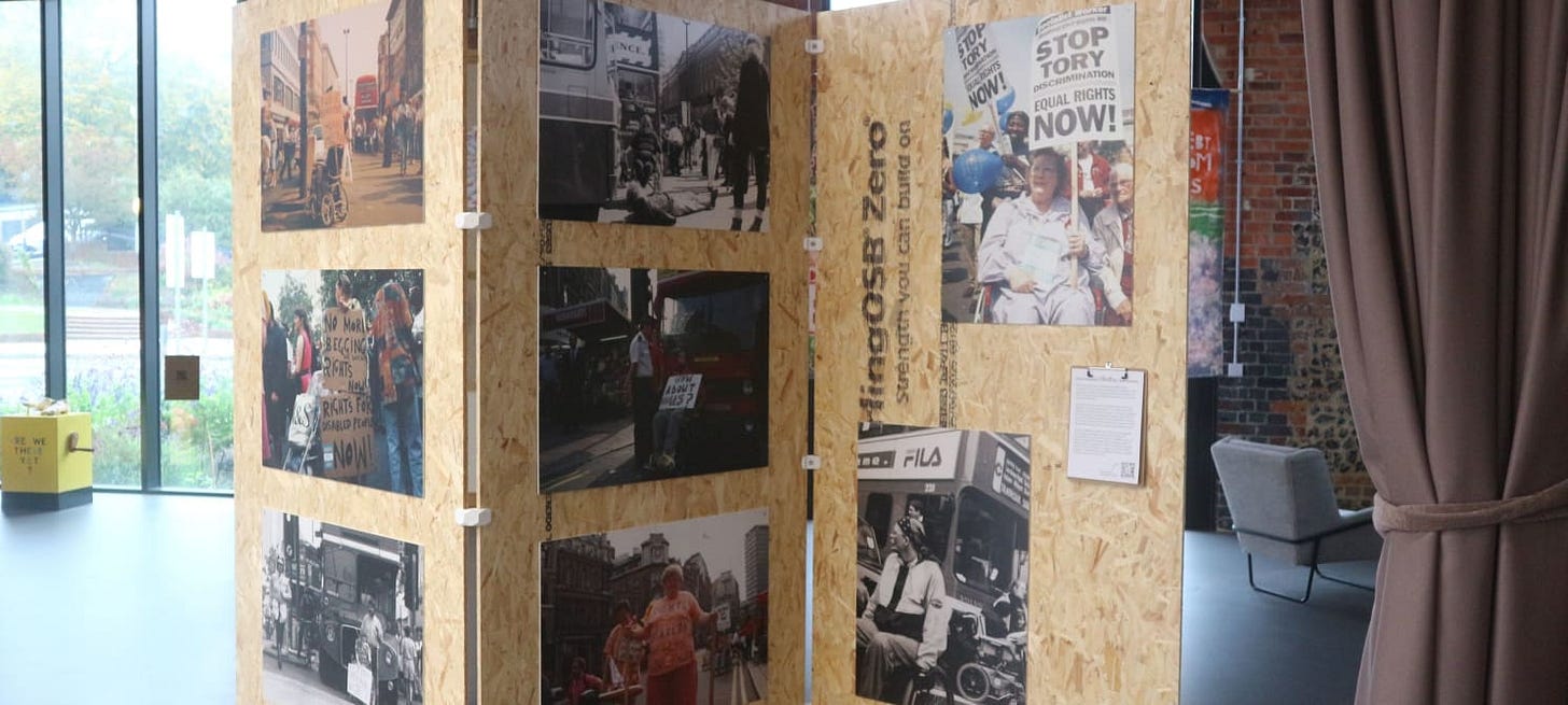 Images of disabled protesters in the streets are hung on a room divider made of plywood.