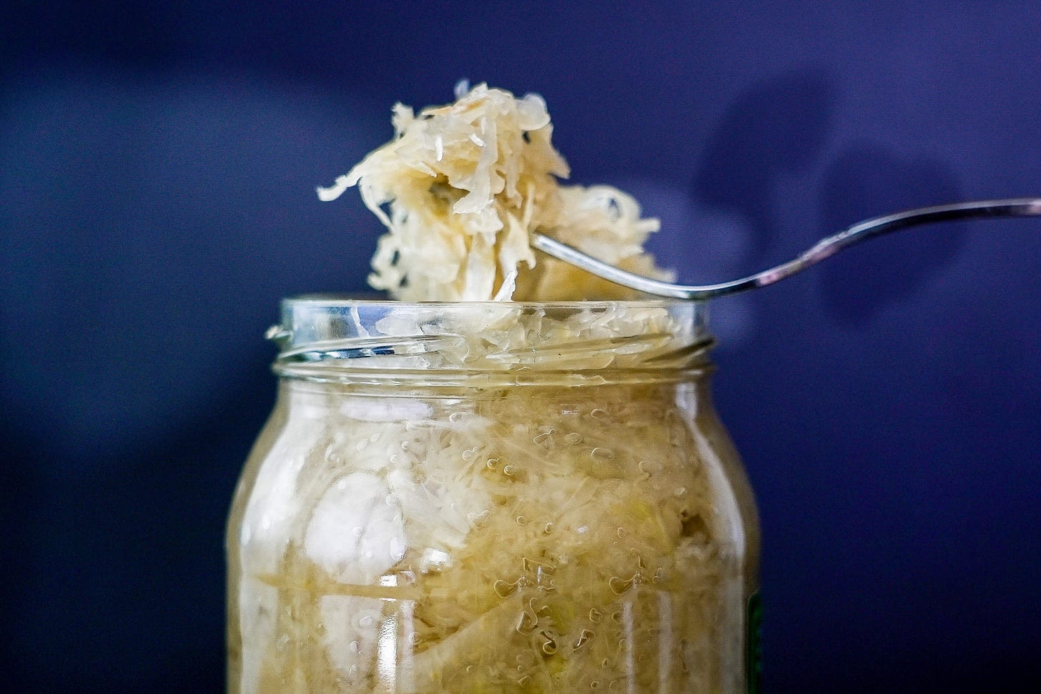 A fork lifting fresh sauerkraut from a glass jar, bubbles visible in the fermented cabbage.
