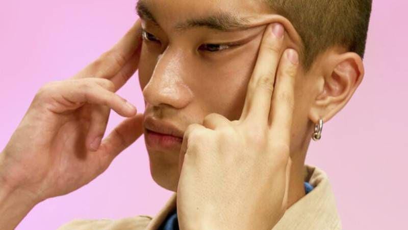Close-up shot of a young Asian man with pulling the corners of his eyes up with both hands.